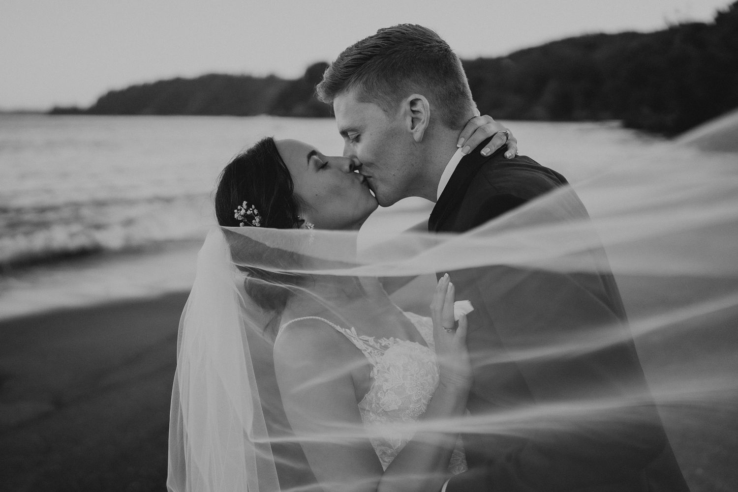 Black and white photo of wedding couple kissing on beach