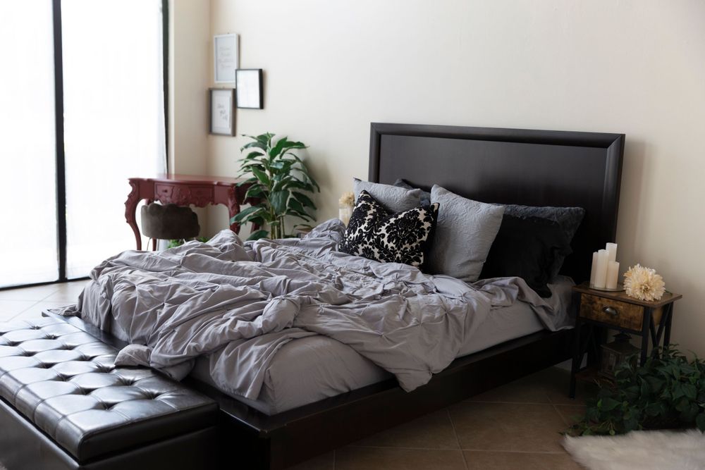 Modern bedroom with gray bedding, black headboard and potted plants.