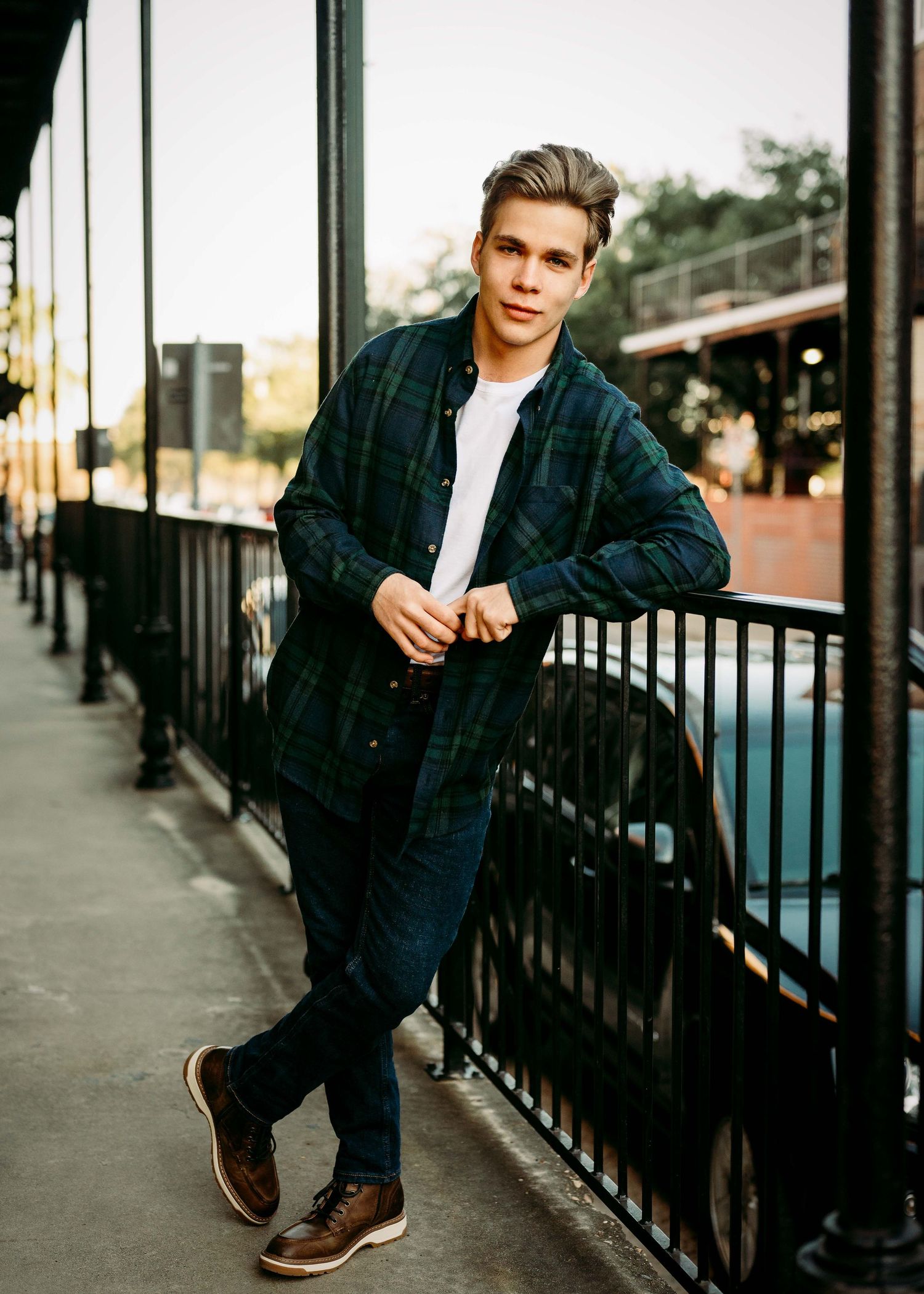 Young man in navy jacket poses casually against black railing during outdoor photo session.