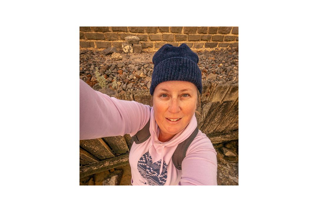 Person wearing pink top and blue beanie takes selfie against brick wall background.
