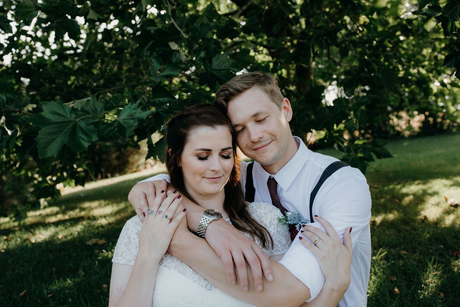 bride and groom hugging with heir eyes closed while sitting under a tree at dusk