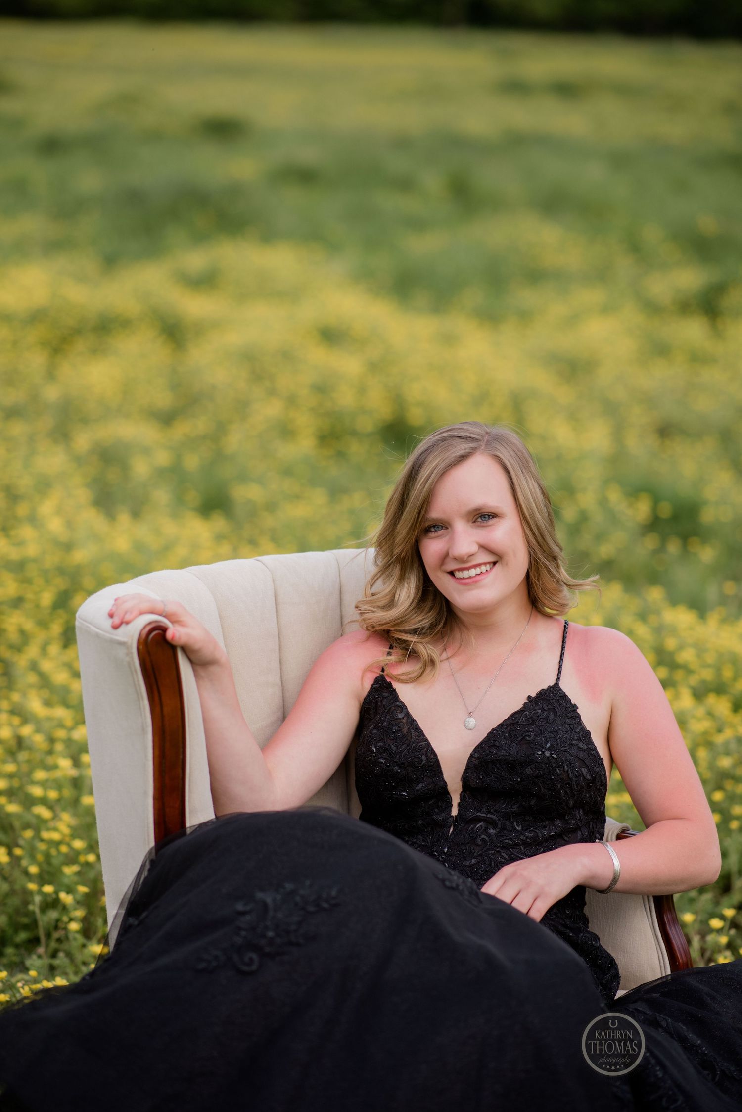 A figure in a black formal dress sits gracefully in a beige armchair surrounded by yellow blooms.