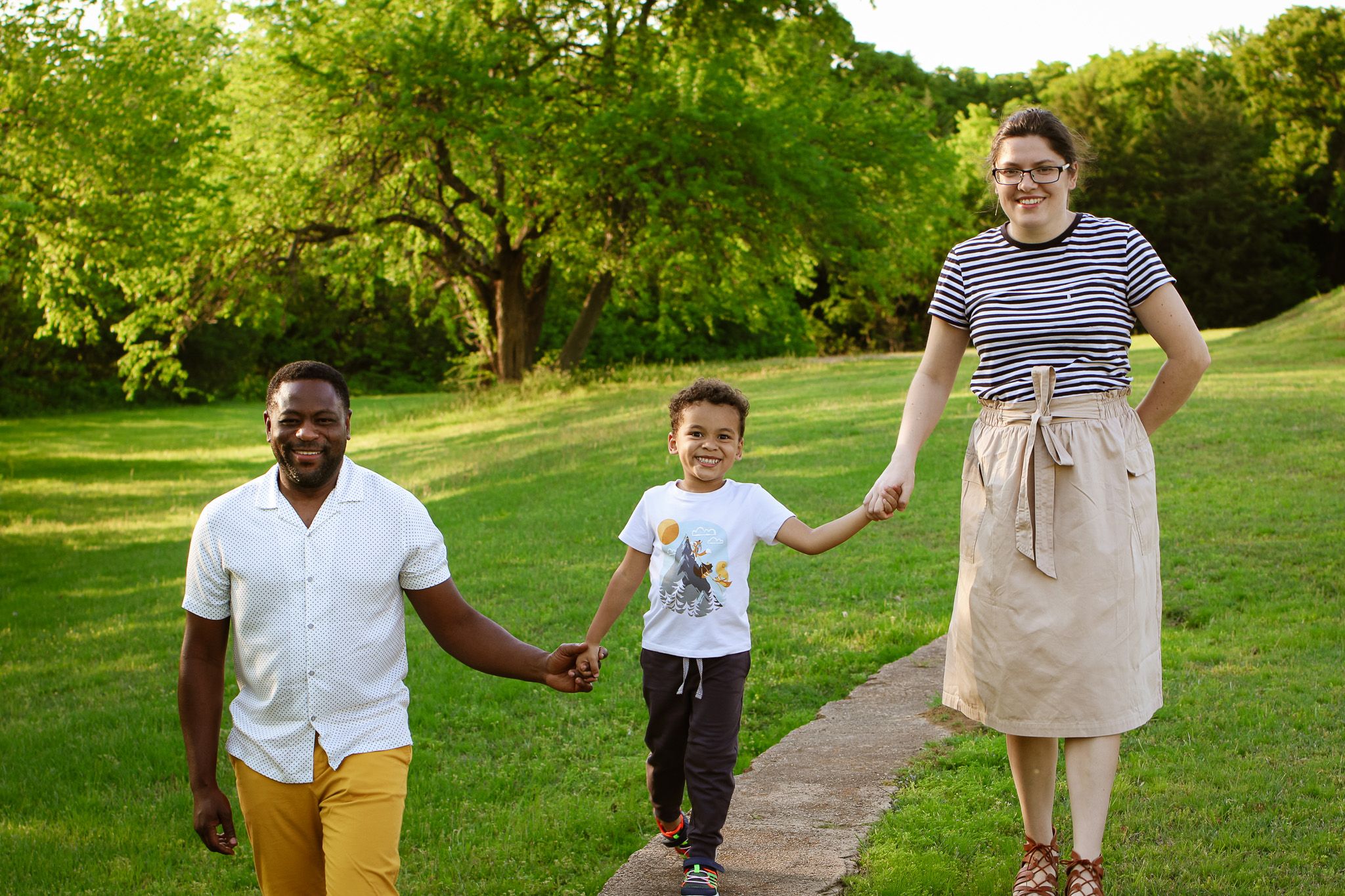 Family walking together on a pathway through a sunny green park.