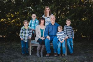 A family portrait outdoors with nature backdrop as they gather on a wooden bench.