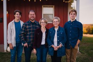 A family of five poses together outside a rustic building with string lights.