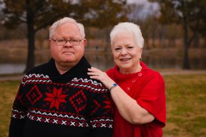 A couple wearing festive winter sweaters poses for a portrait outdoors.