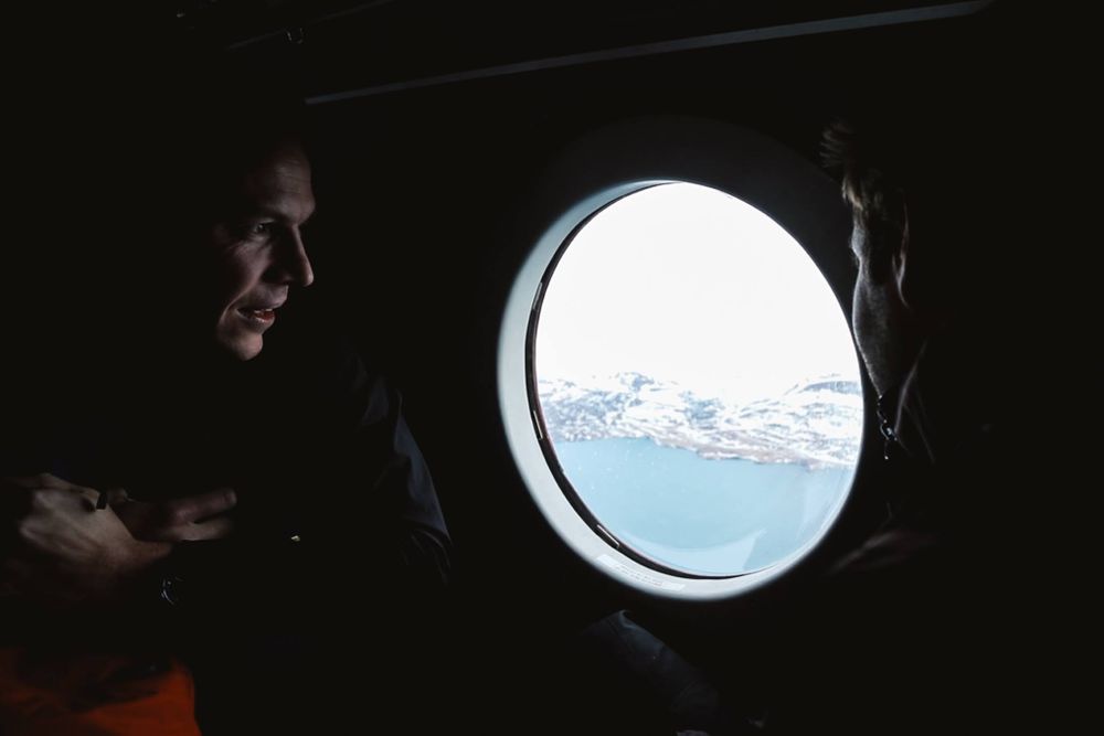 two adventurers looking out of a small round plane window onto a snowy backdrop