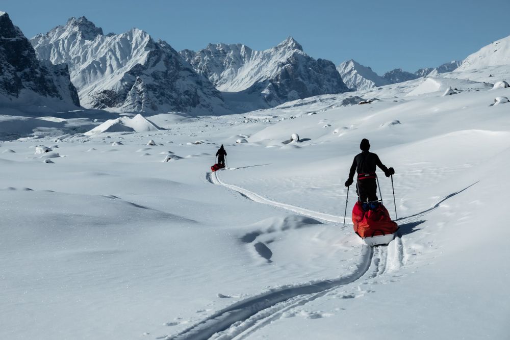 Two splitboarders pulling pulks towards large snowy mountains in the Stauning Alps