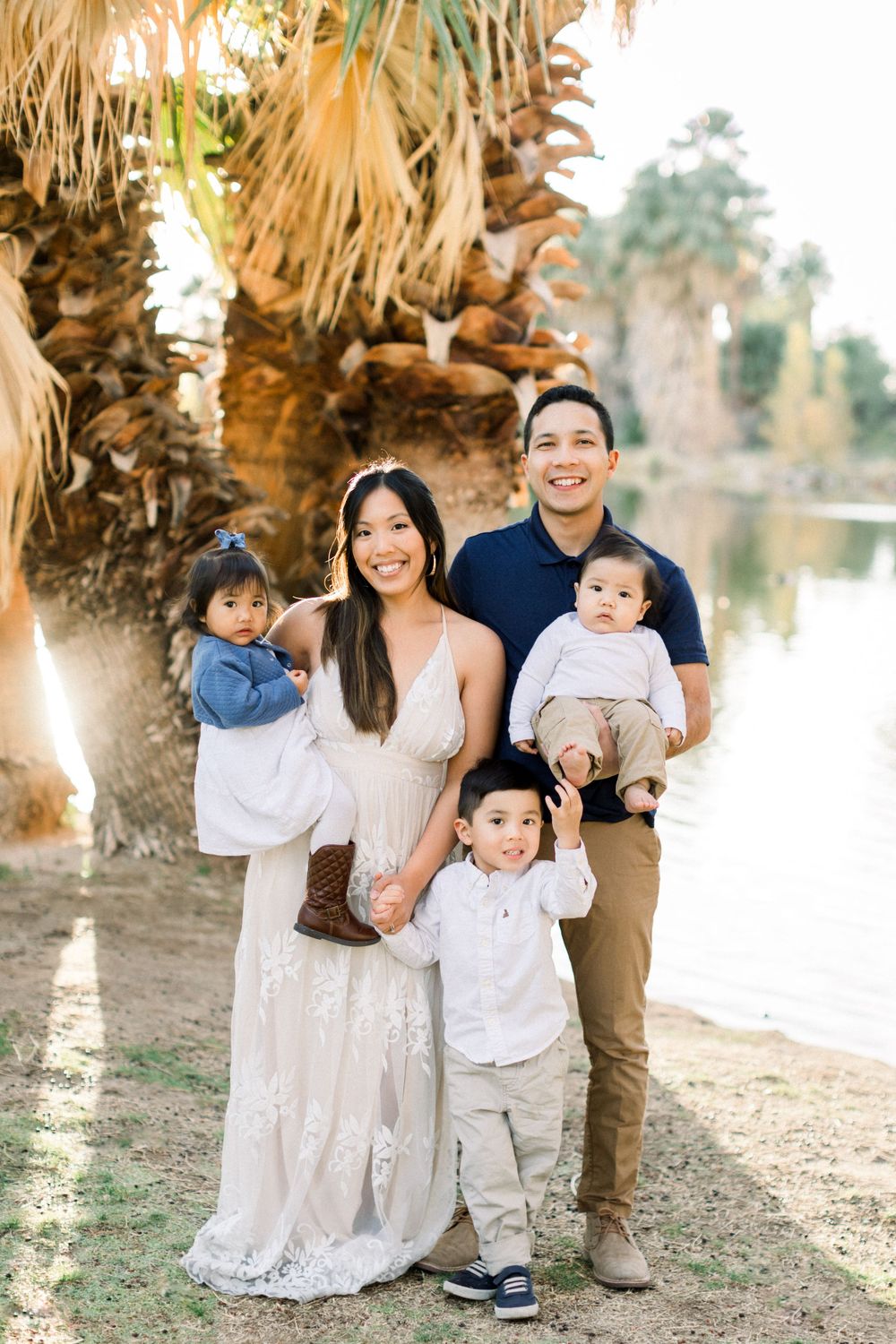 A family poses together near a palm tree-lined lake at sunset.