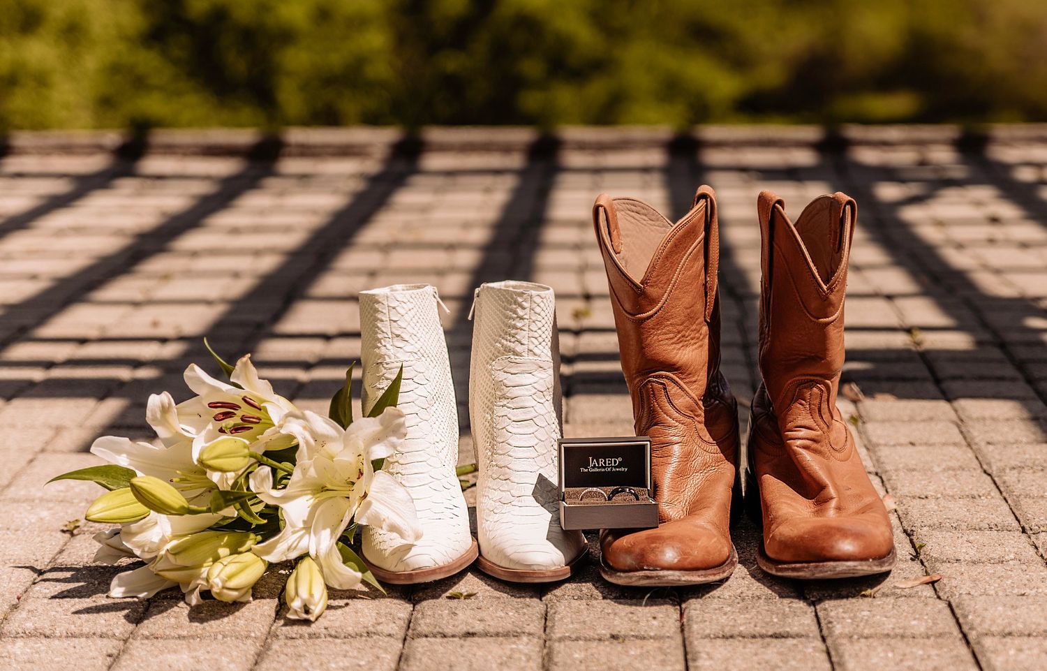White and brown cowboy boots lined up on brick pavement with scattered autumn leaves.