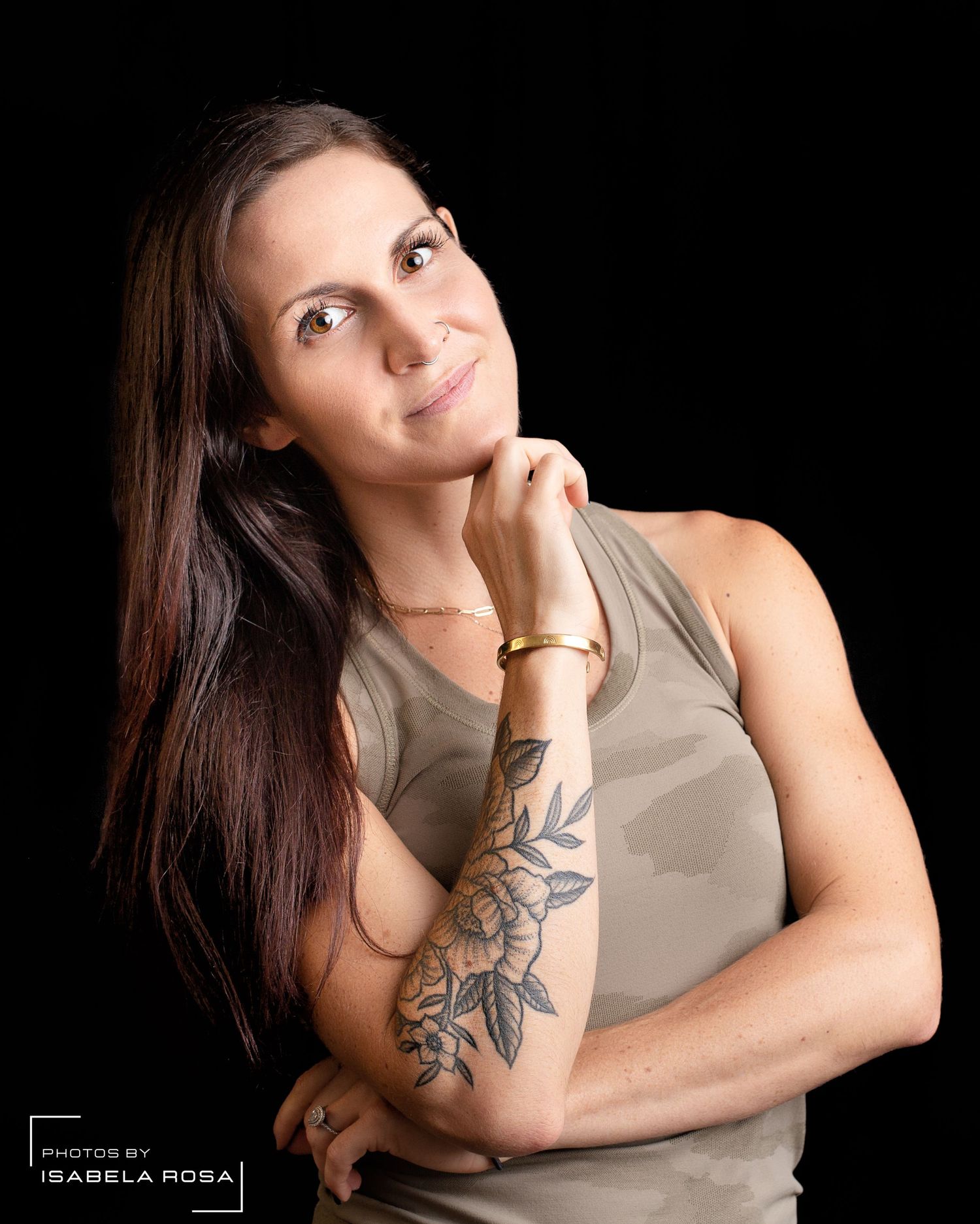 Portrait of athletic woman with floral arm tattoo posing against black background.