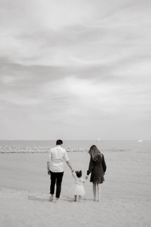 A family walks along the beach holding hands in black and white.