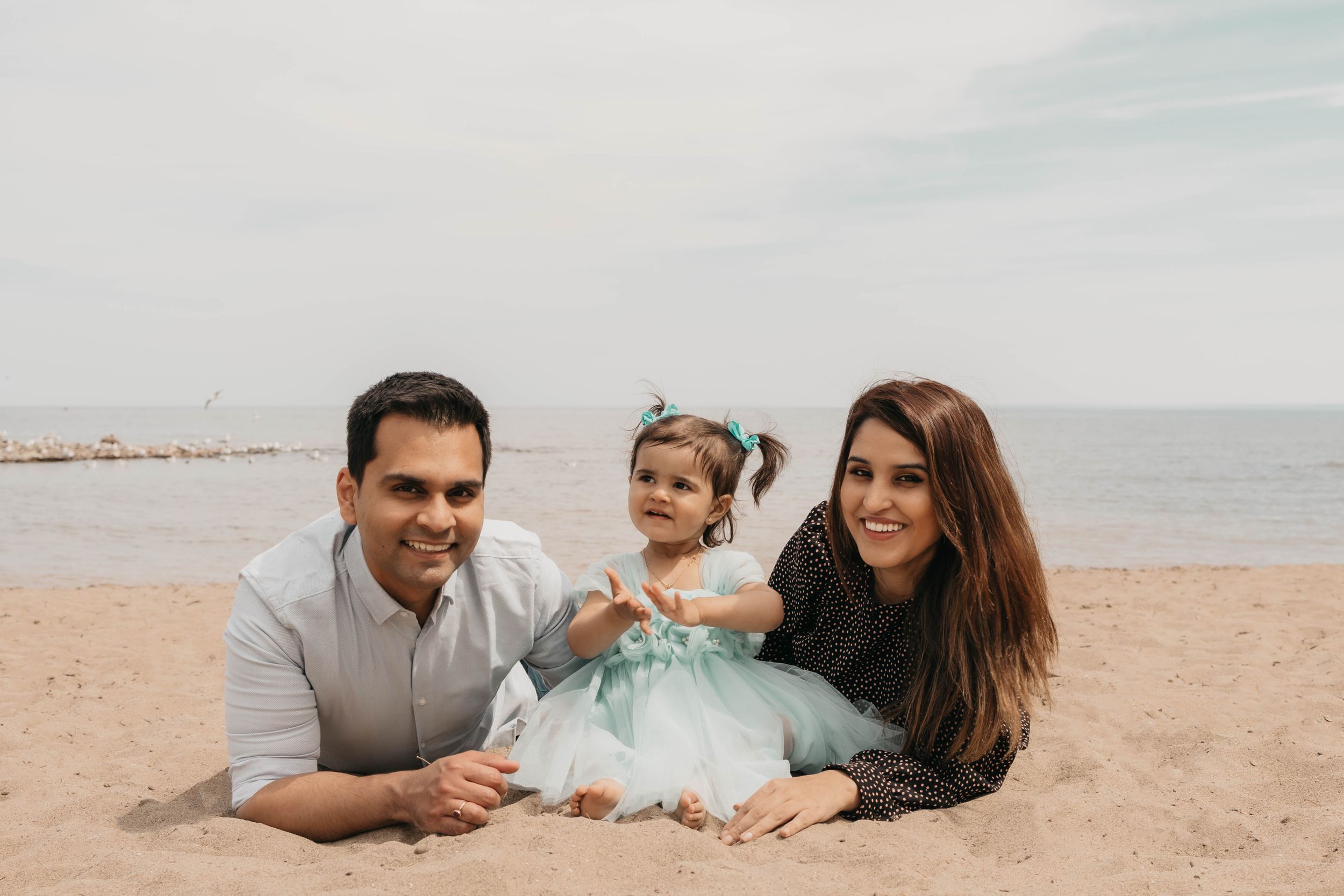 A family poses together while lying on the sand at the beach.