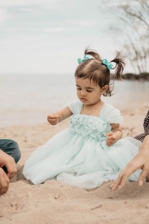 A small child in a mint tulle dress plays in the sand at the beach.