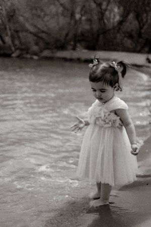 A black and white photo of a child exploring the beach in a white dress.