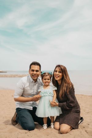 Family portrait on sandy beach with toddler in light blue dress.