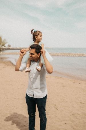 Father carries child on shoulders during beach photoshoot.