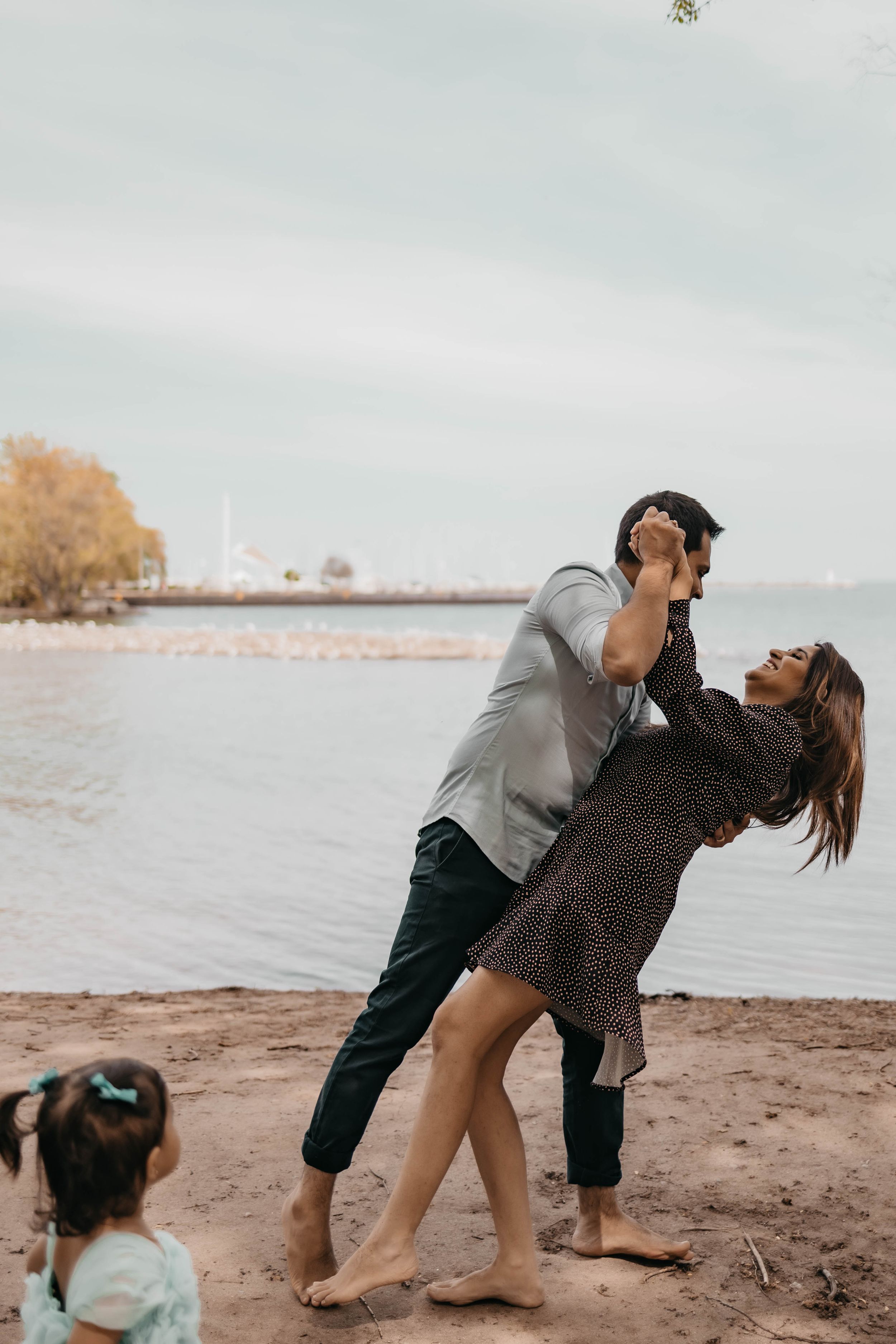 A romantic dance moment captured on a beach with a little one watching in the background.