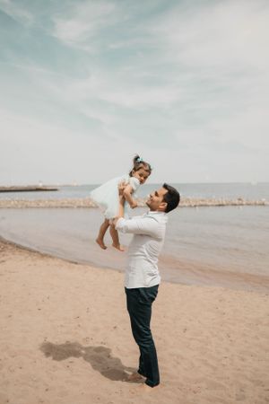 A joyful moment captured as a parent lifts a child in the air at the beach.