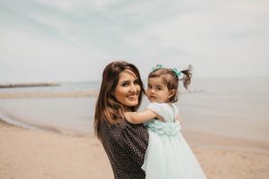 Mother lifts daughter in aqua dress during beach photoshoot.