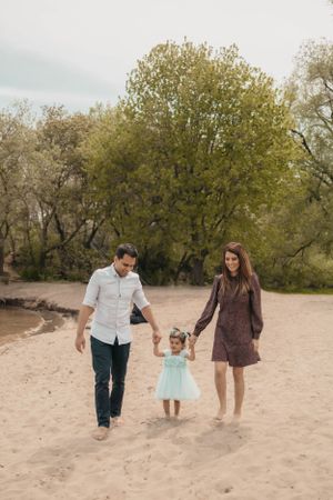 A family walks hand in hand along a sandy beach with trees in the background.
