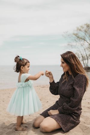 A tender moment captured on a beach as a child in a mint dress dances with a companion in a polka dot dress.