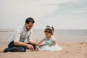 A parent and child in a mint dress play together in the sand at the beach.