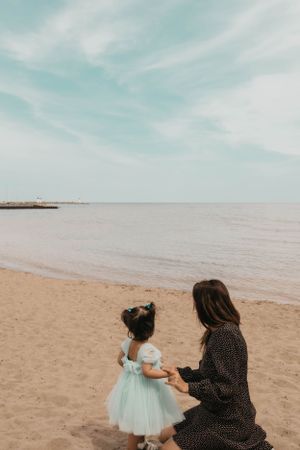 Mother and daughter in tulle dress share moment on peaceful beach.