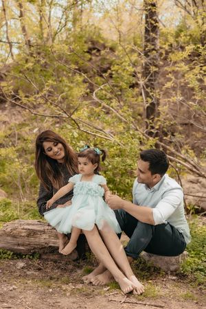 A family shares a joyful moment together while sitting on a fallen tree in a wooded setting.