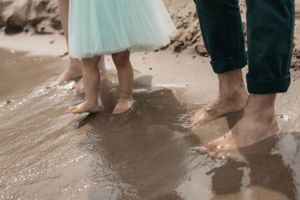 Bare feet standing in wet sand at the edge of the water.