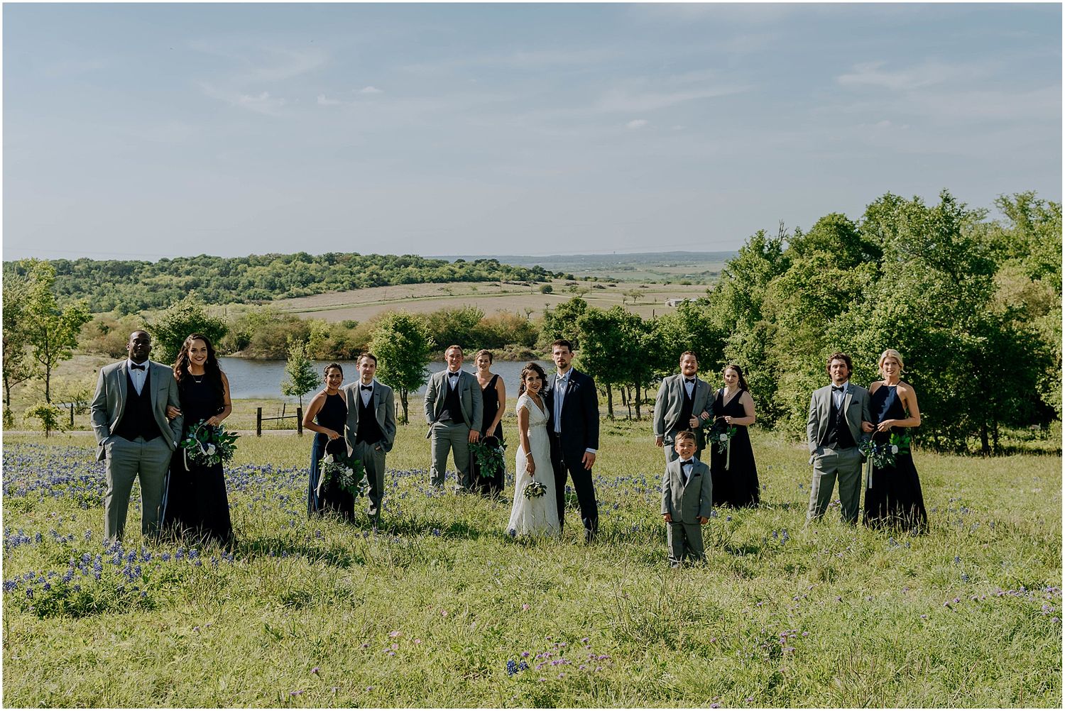 Wedding party poses on hilltop with scenic countryside views in background.
