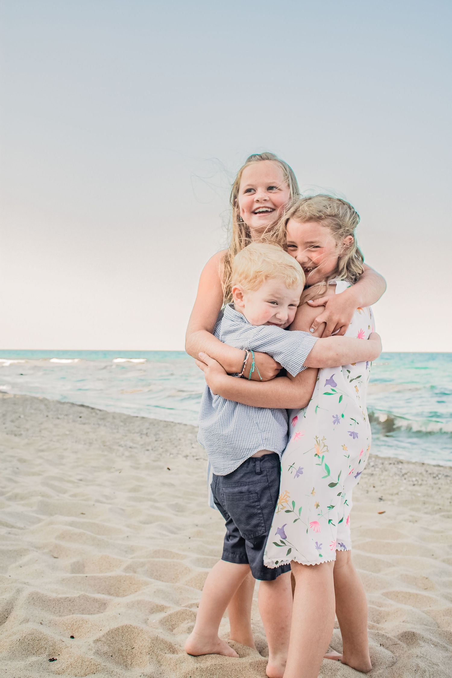 Three people share a joyful embrace on a sandy beach at sunset.