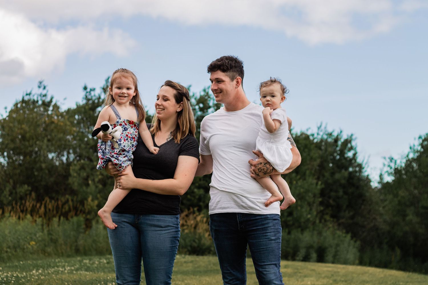 Family walking together through green field under blue sky.