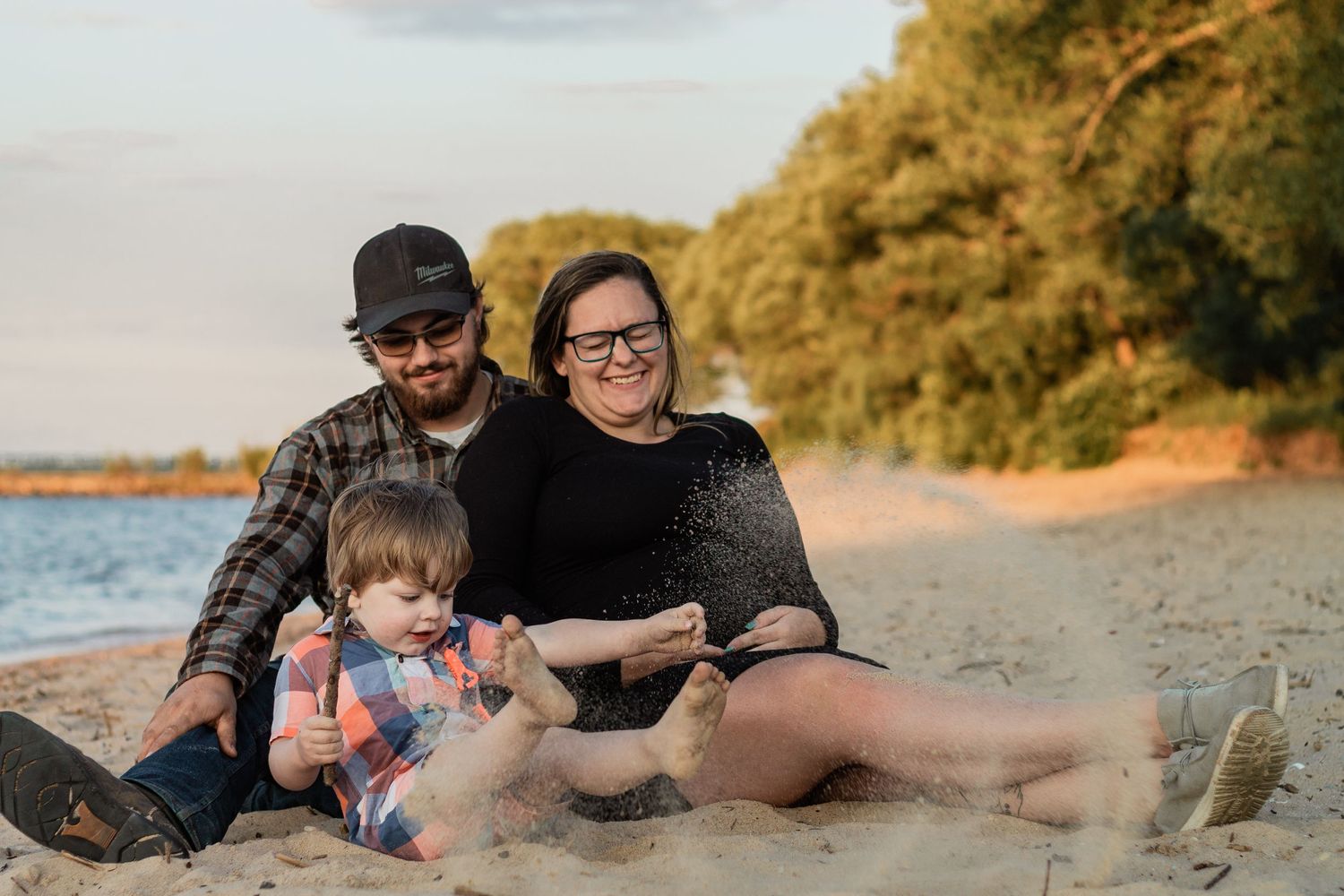 Family sitting together on sandy beach at sunset with trees in background.