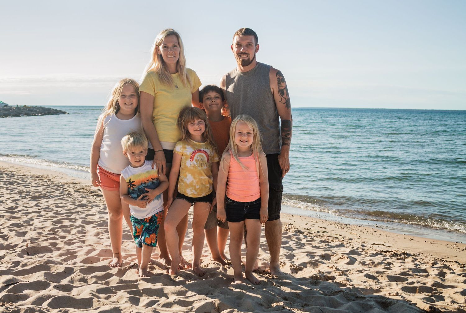 Group portrait on sunny beach with ocean waves and blue sky in background.