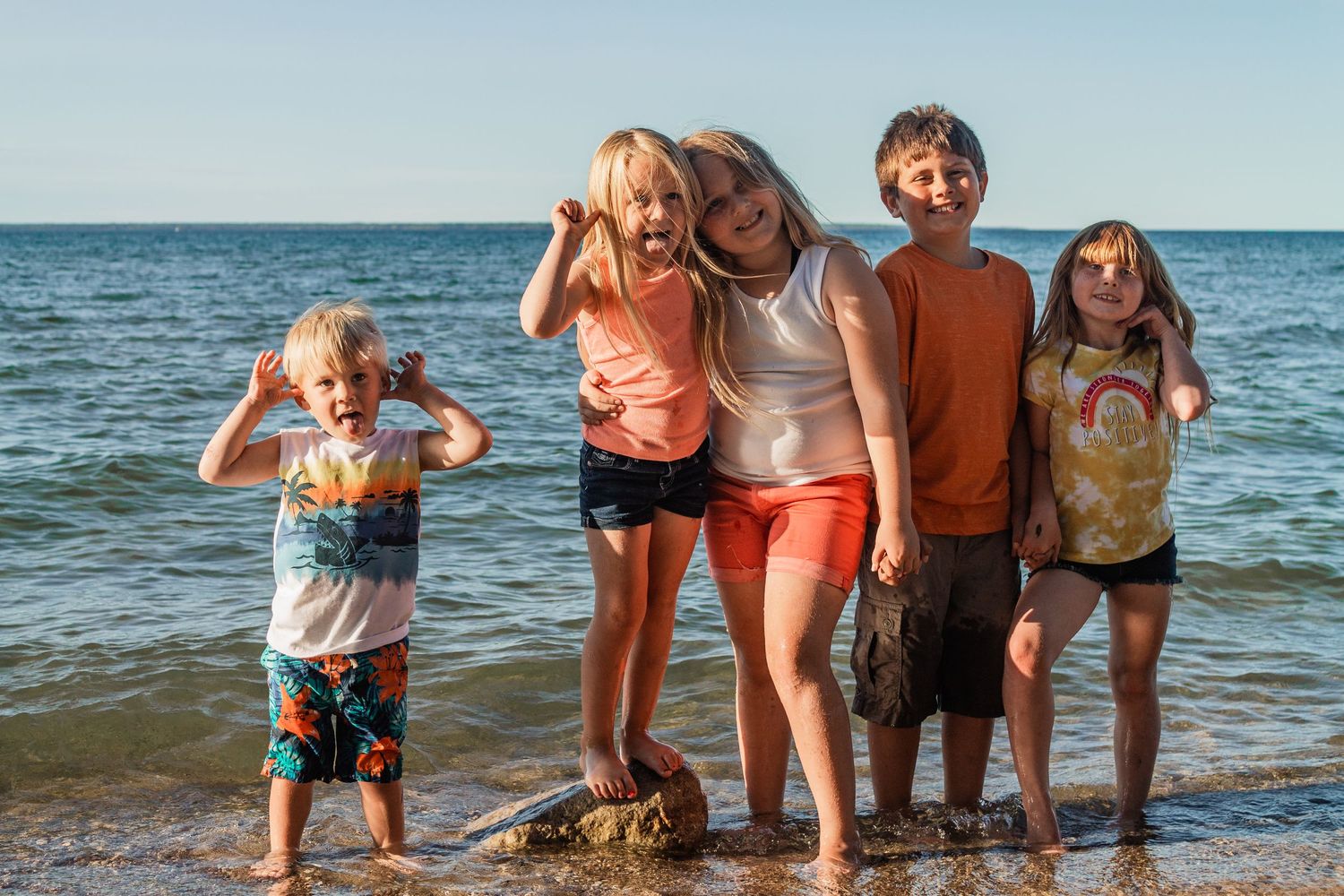 Group posing playfully on beach with ocean waves in background.