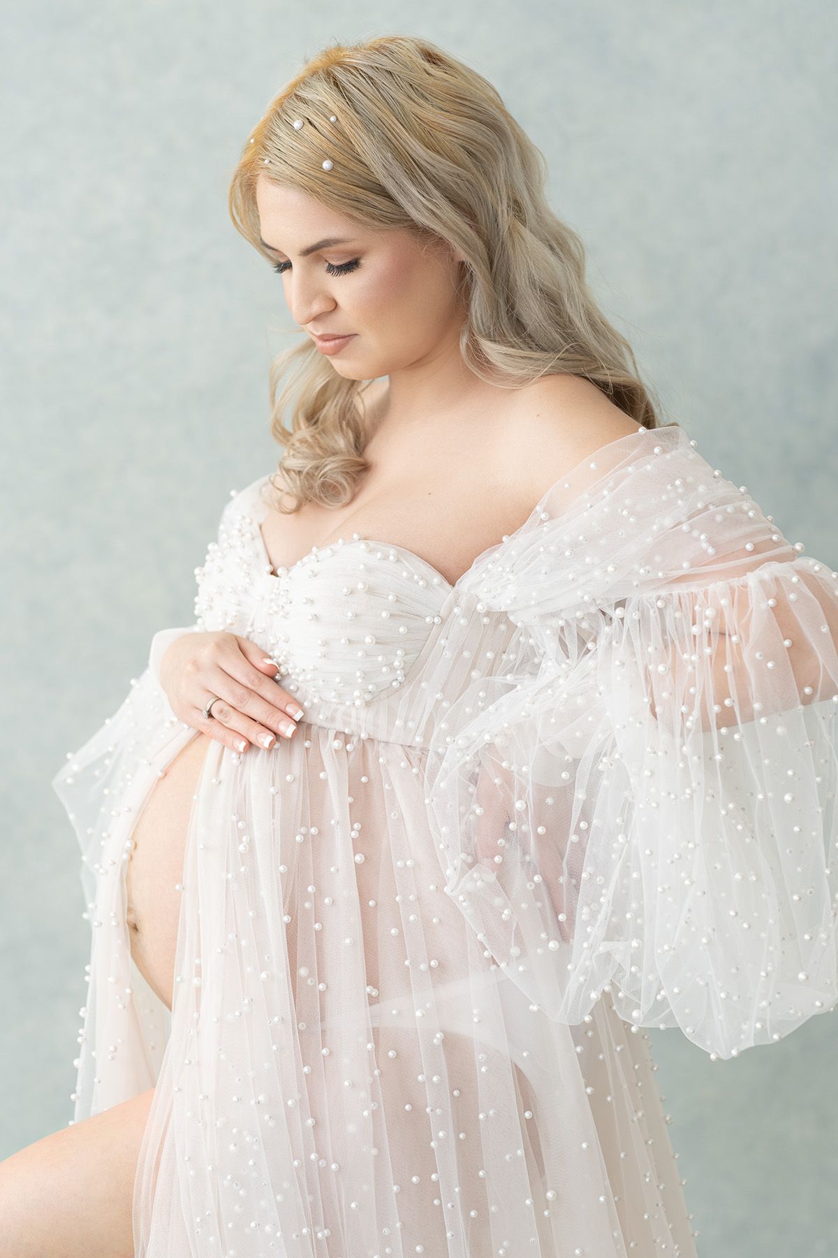 A dreamy maternity portrait featuring a sheer white pearl-embellished robe with flowing sleeves against a soft gray backdrop. Minneapolis