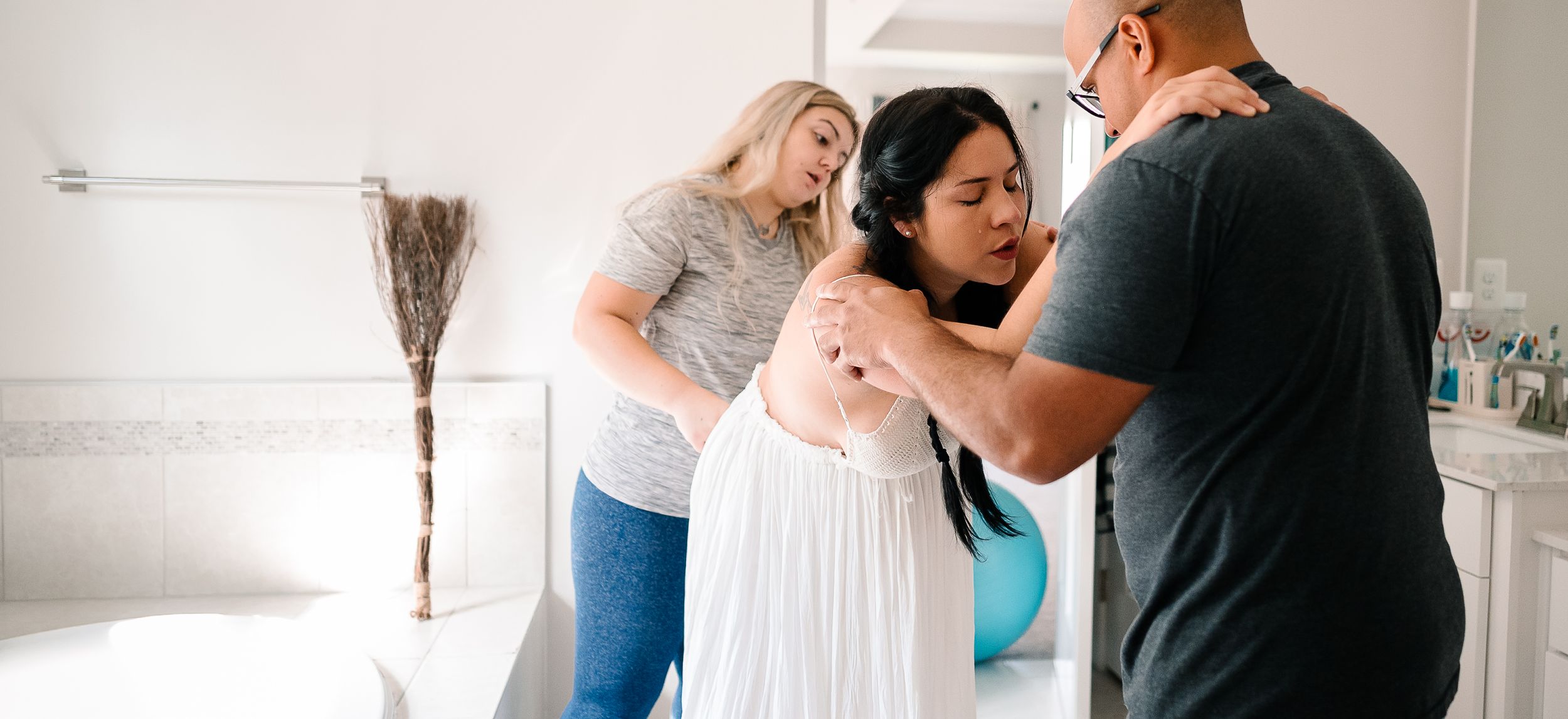 Pregnant woman laboring In Bathroom With Doula and Husband supporting her back and shoulders