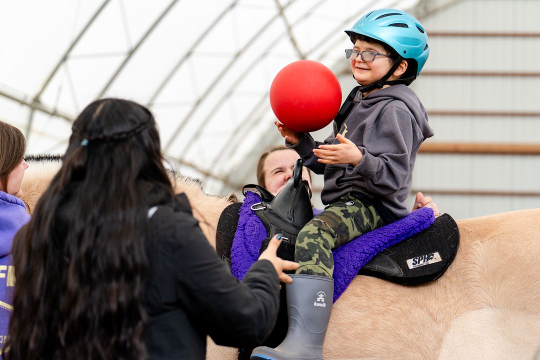 boy catches a ball while sitting on a horse
