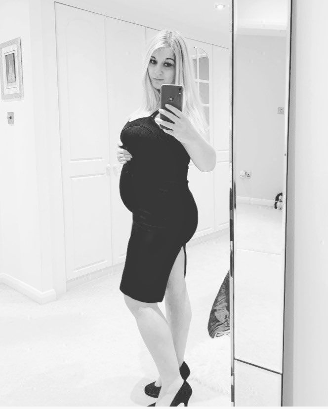 A maternity mirror selfie showing a black dress silhouette against white interior.