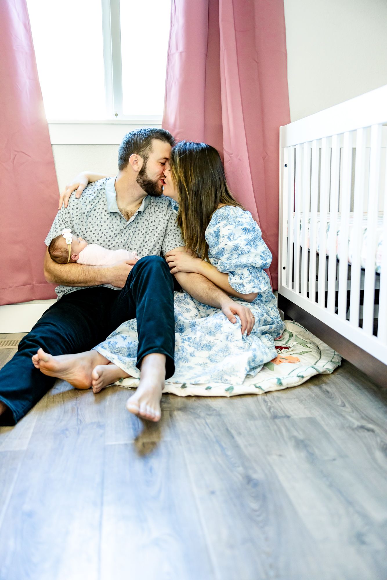 Parents sit on the floor kissing while dad holds baby girl during newborn photos in Colorado Springs.