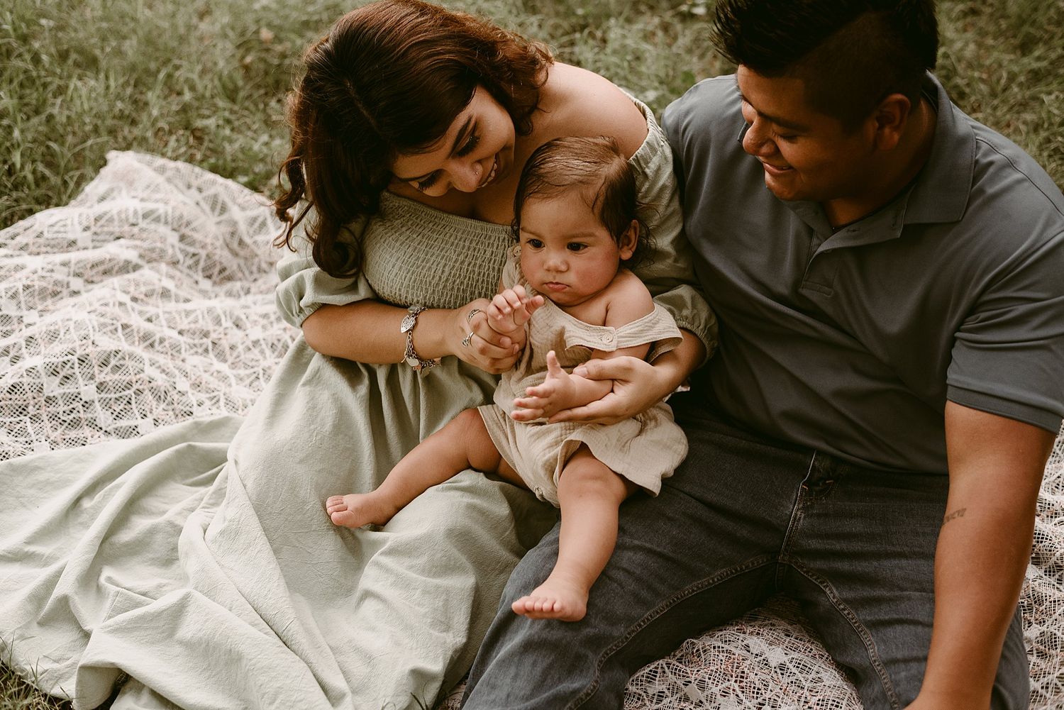Intimate family portrait on white lace blanket during outdoor photo session.