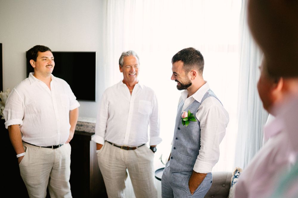 Groomsmen in white shirts and grey attire having a pre-wedding conversation.