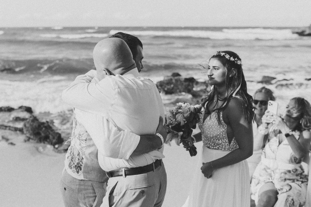 Black and white photo of beachside wedding ceremony with rocky coastline.