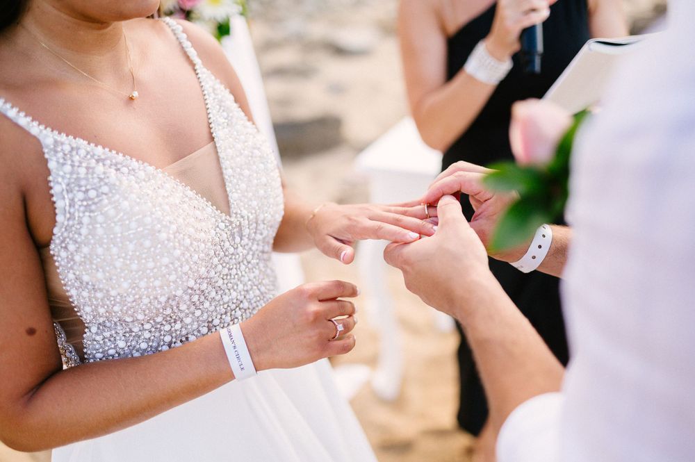 Close-up shot of wedding rings being exchanged during a beachside ceremony.