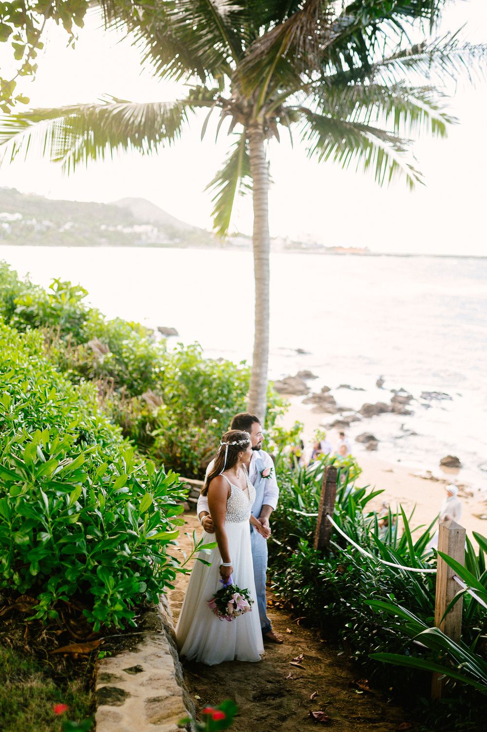 A romantic portrait under a palm tree on a tropical beach with ocean views.