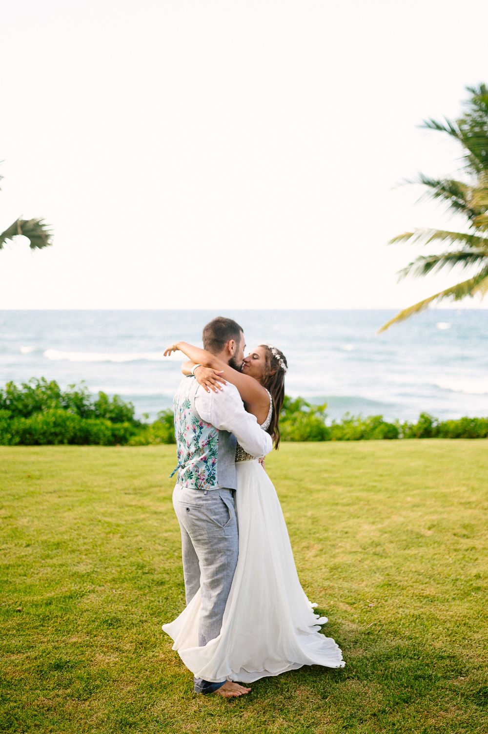 A romantic embrace on a green lawn overlooking the tropical ocean.