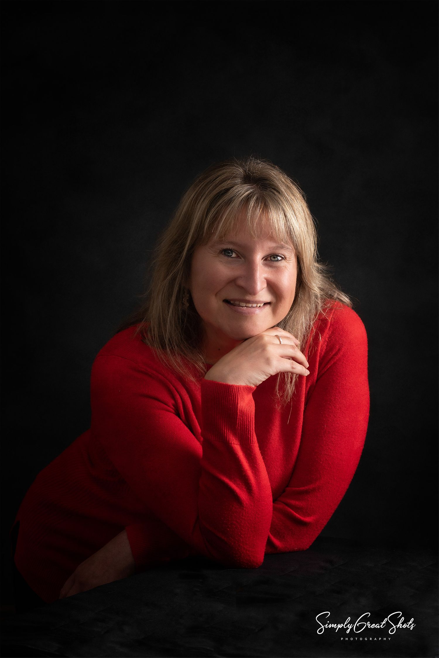 A studio portrait photograph of a lady posing in a red sweater
