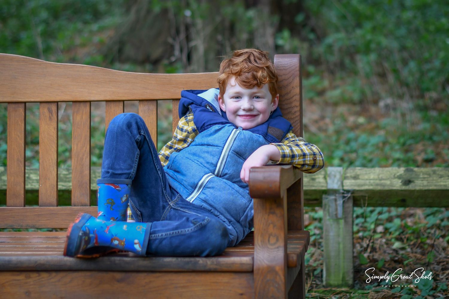 A outdoor family photoshoot - A ginger haired boy sitting on a park bench