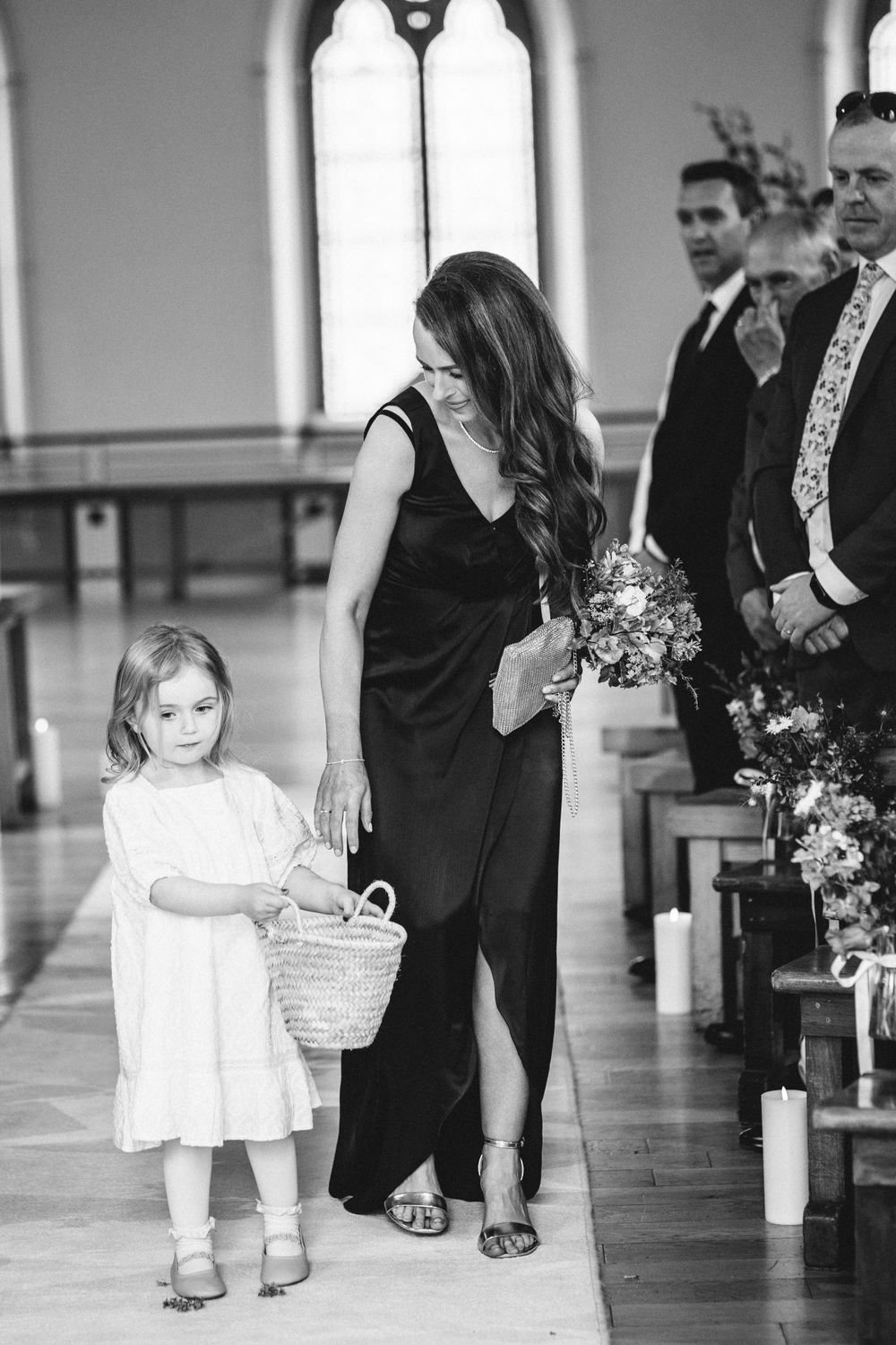 Black and white photo of wedding processional with small child in white dress walking down church aisle.